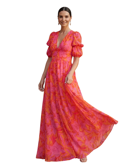 Modelo con vestido maxi Mara Domínguez de gasa floral rosa y naranja, escote en V y mangas abullonadas en exterior.