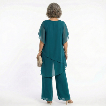 Vista trasera del conjunto Mara Domínguez Ainhoa en verde azulado con blusa de capas y pantalón fluido para eventos.
